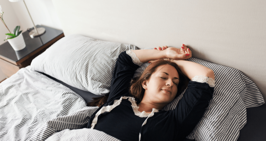 A woman lying on her back in bed with her arms resting above her head and her eyes closed