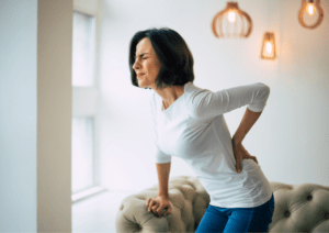 A woman with back hair wearing a white t-shirt in pain because of her back.