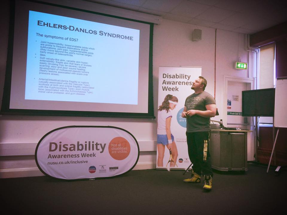 A man stood infant of a projector with a titles screen for disability awareness week