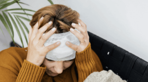 A woman with blonde hair, with a headache wearing a yellow jumper
