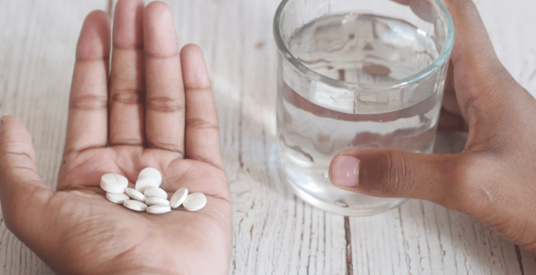 a woman's hand holding the medication gabapentin, whilst her other hand hold a glass of water