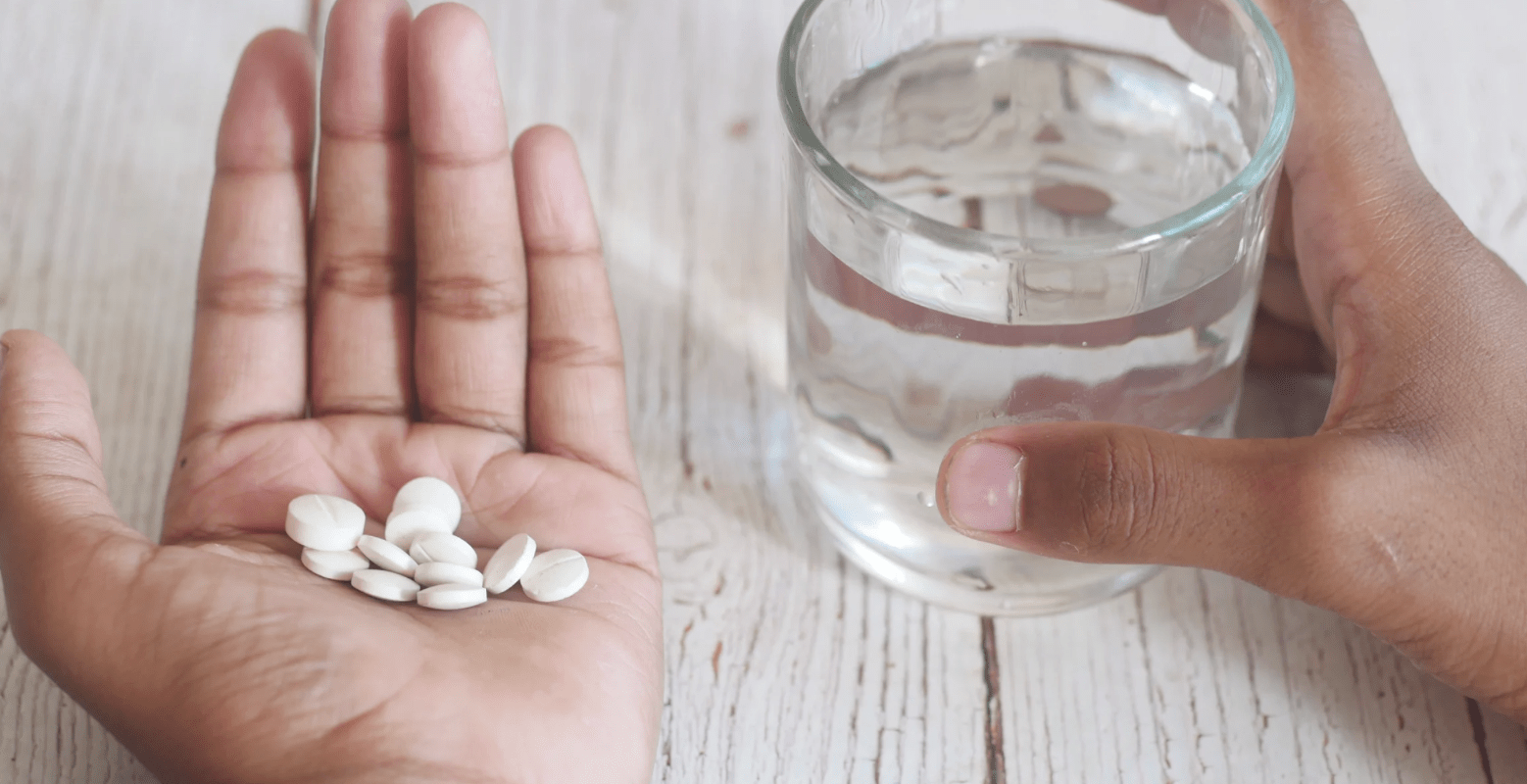 a woman's hand holding the medication gabapentin, whilst her other hand hold a glass of water