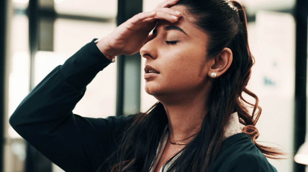 A woman standing with her eyes shut and one hand pressed to her forehead